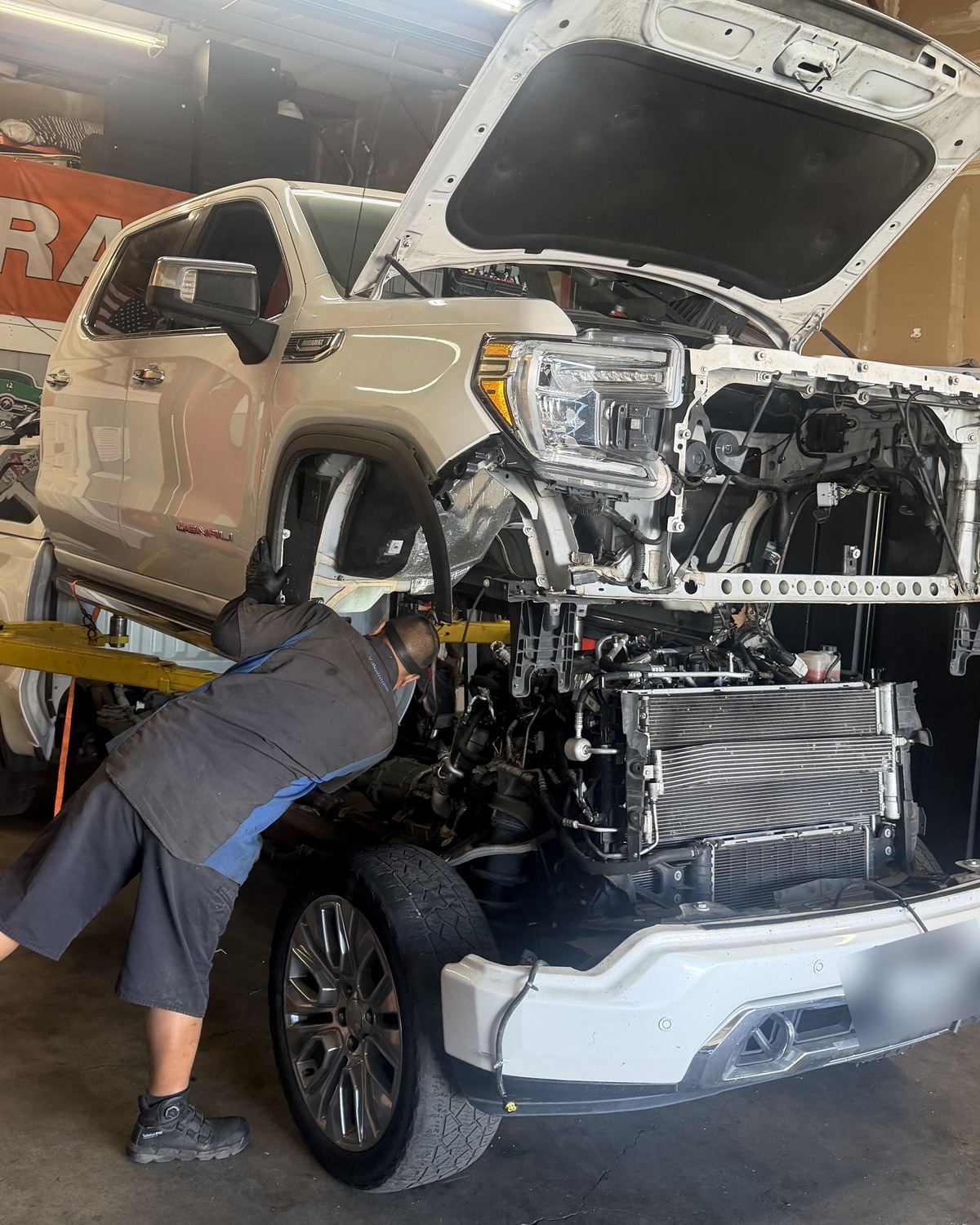 A mechanic working under a white GMC Sierra on the lift at Ronnie’s Automotive in Sacramento, with the truck’s front end taken apart