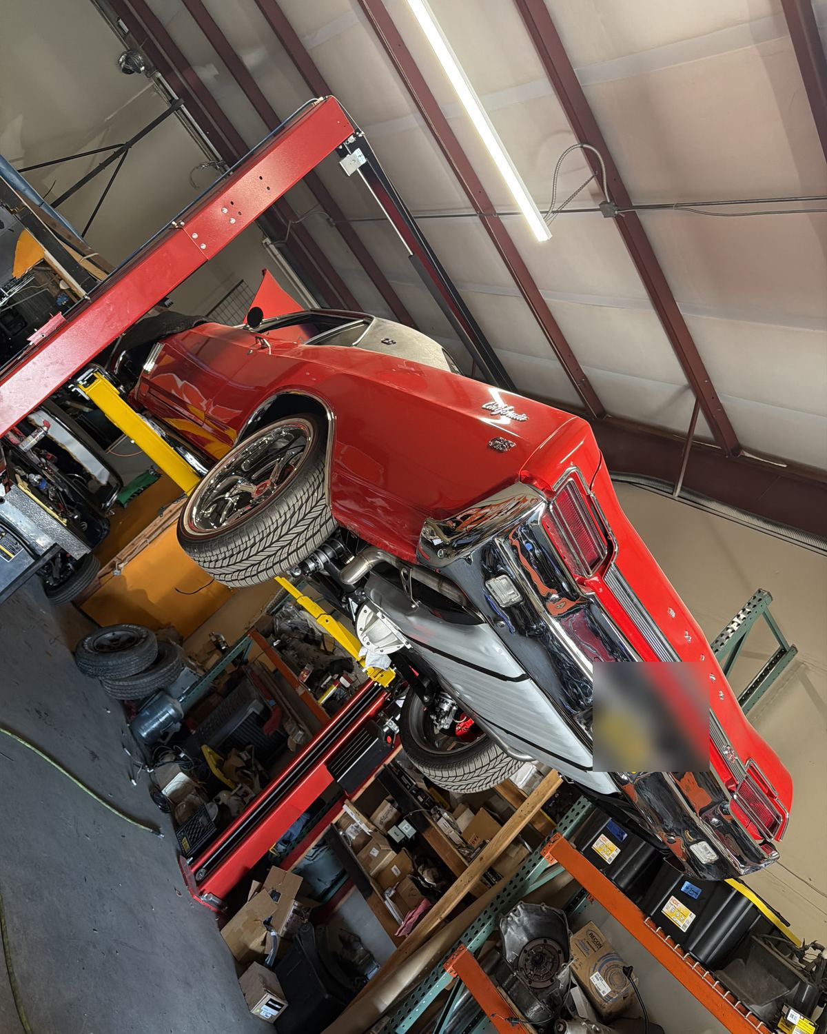 A red classic car raised on a lift in the shop at Ronnie’s Automotive