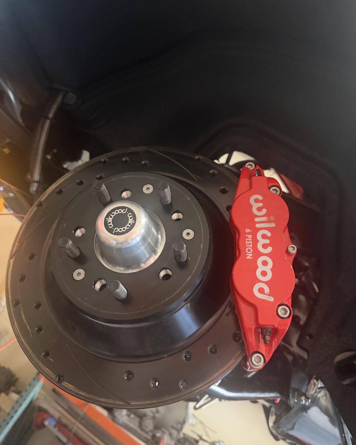 A drilled disc brake rotor with a red Wilwood caliper on a classic car at Ronnie’s Automotive